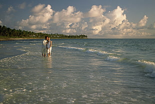 photo of man and woman standing on sea near forest trees